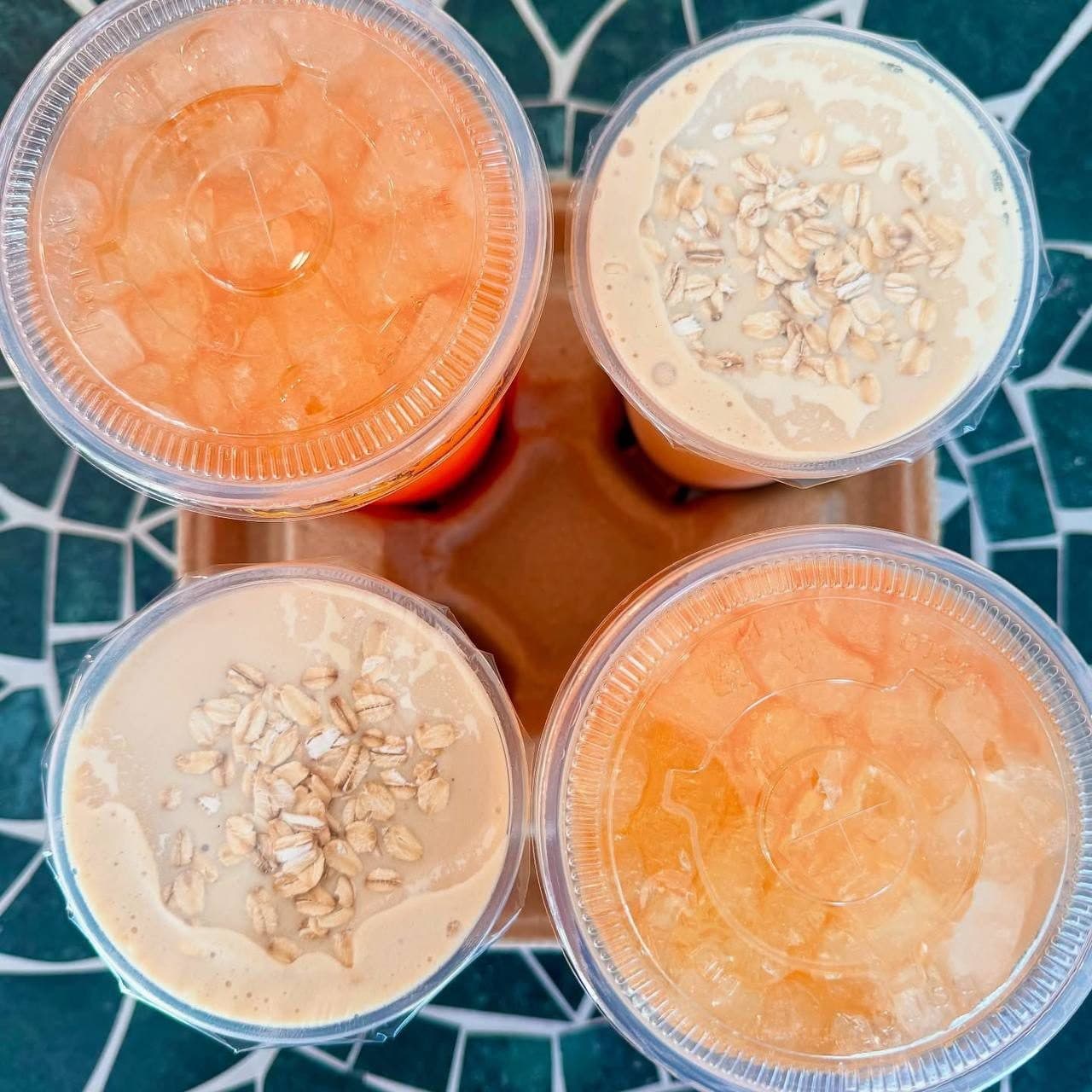 A to-go carrier with four drinks — peach teas and oat-topped shakes — on a mosaic table