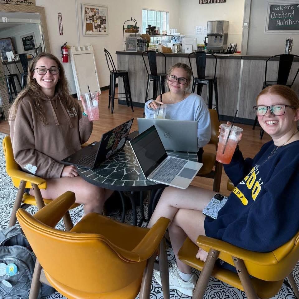 Three friends studying with laptops and loaded teas at a table inside Orchard Nutrition